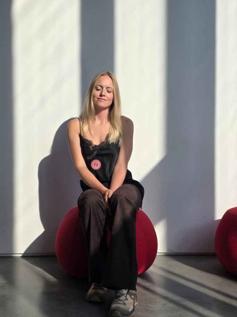 Портрет дизайнера: светловолосая женщина в спокойной позе на красном кресле-мешке, освещённая естественным светом